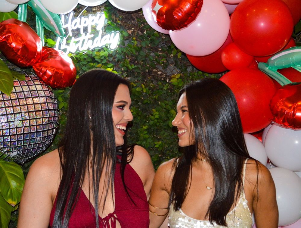 Dos personas riéndose frente a globos de cumpleaños